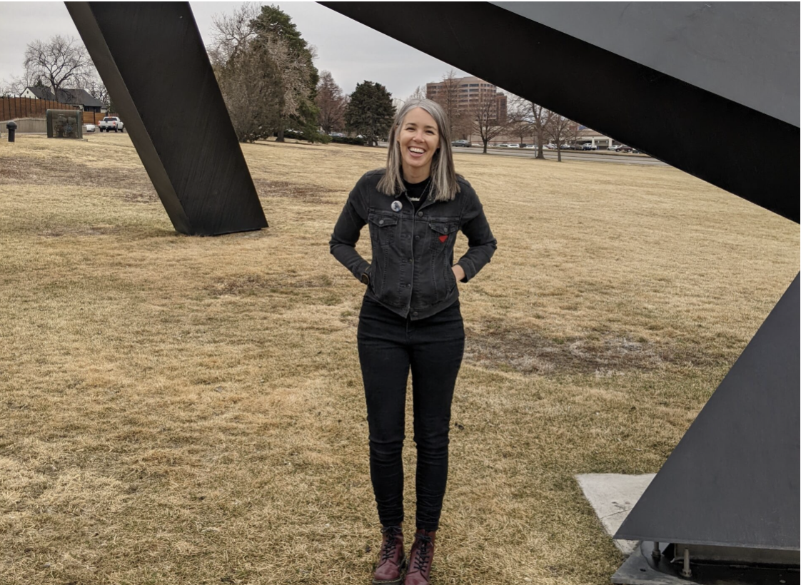 Alison is standing outside in front of a large black sculpture at a park.